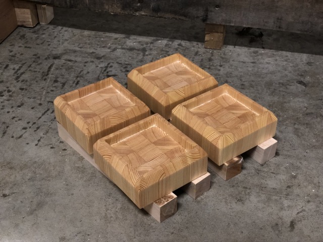 Four freshly oiled identical square blocks of wood resting an inch above a concrete floor.